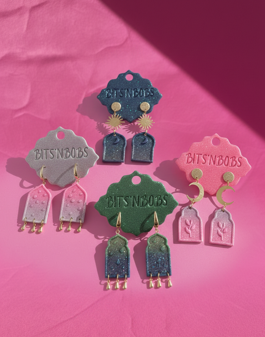 Colorful earrings with 'BITS'NBOBS' branding on pink and purple background