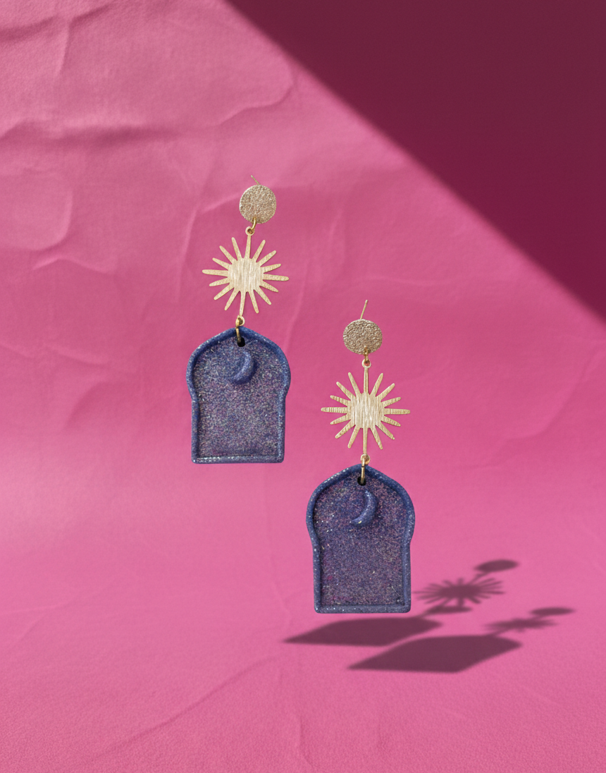 A pair of glittery blue earrings adorned with gold plated textured findings and a celestial charm